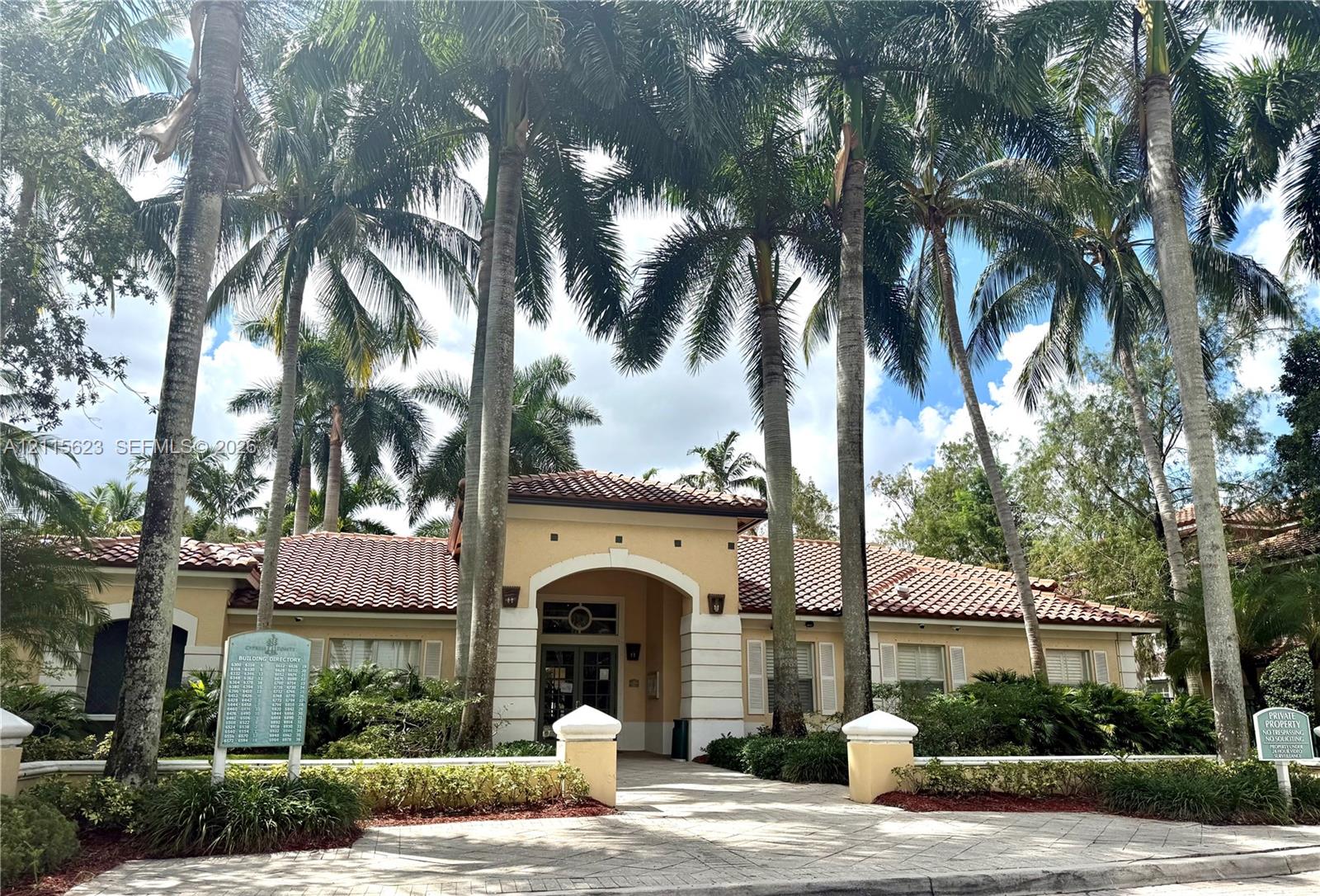 Stucco exterior featuring a tiled roof, arched entryway, and patterned paver walkway, surrounded by mature palm trees