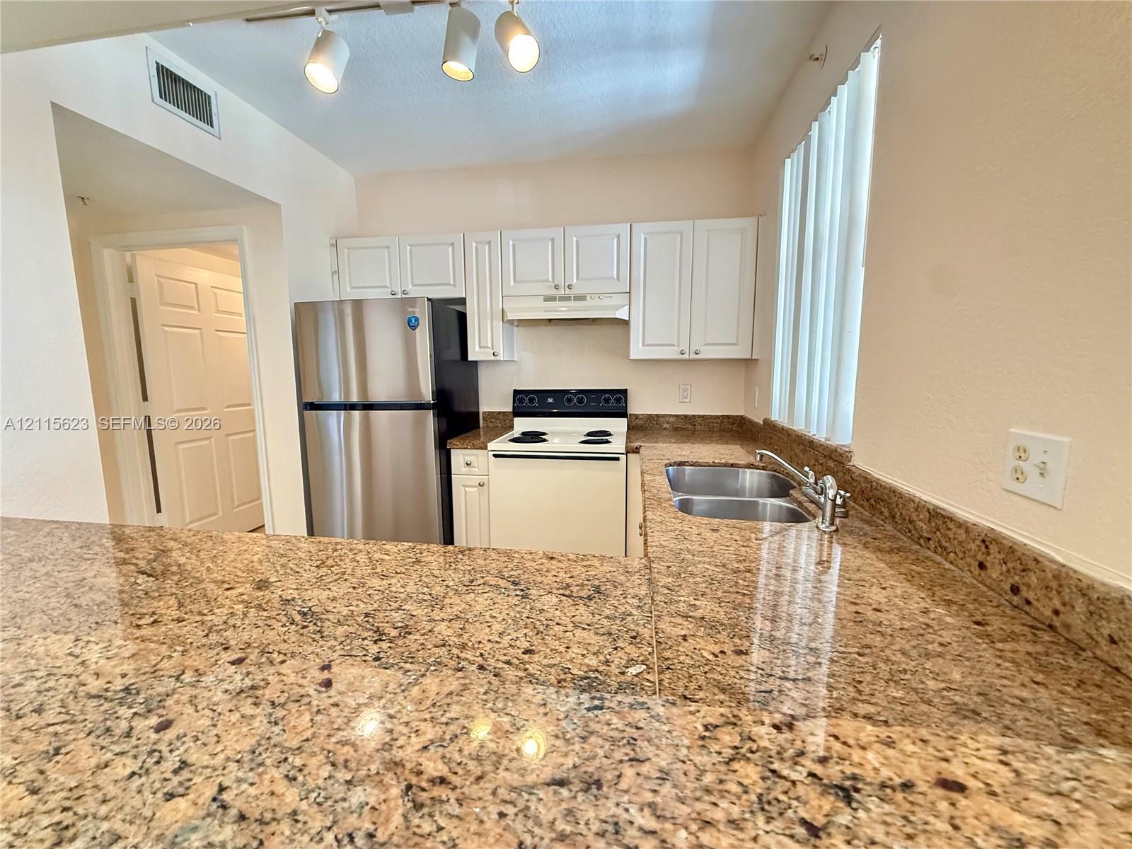 Kitchen featuring stone countertops, white cabinetry, a stainless steel refrigerator, a white electric range, and a dual-basin stainless steel sink