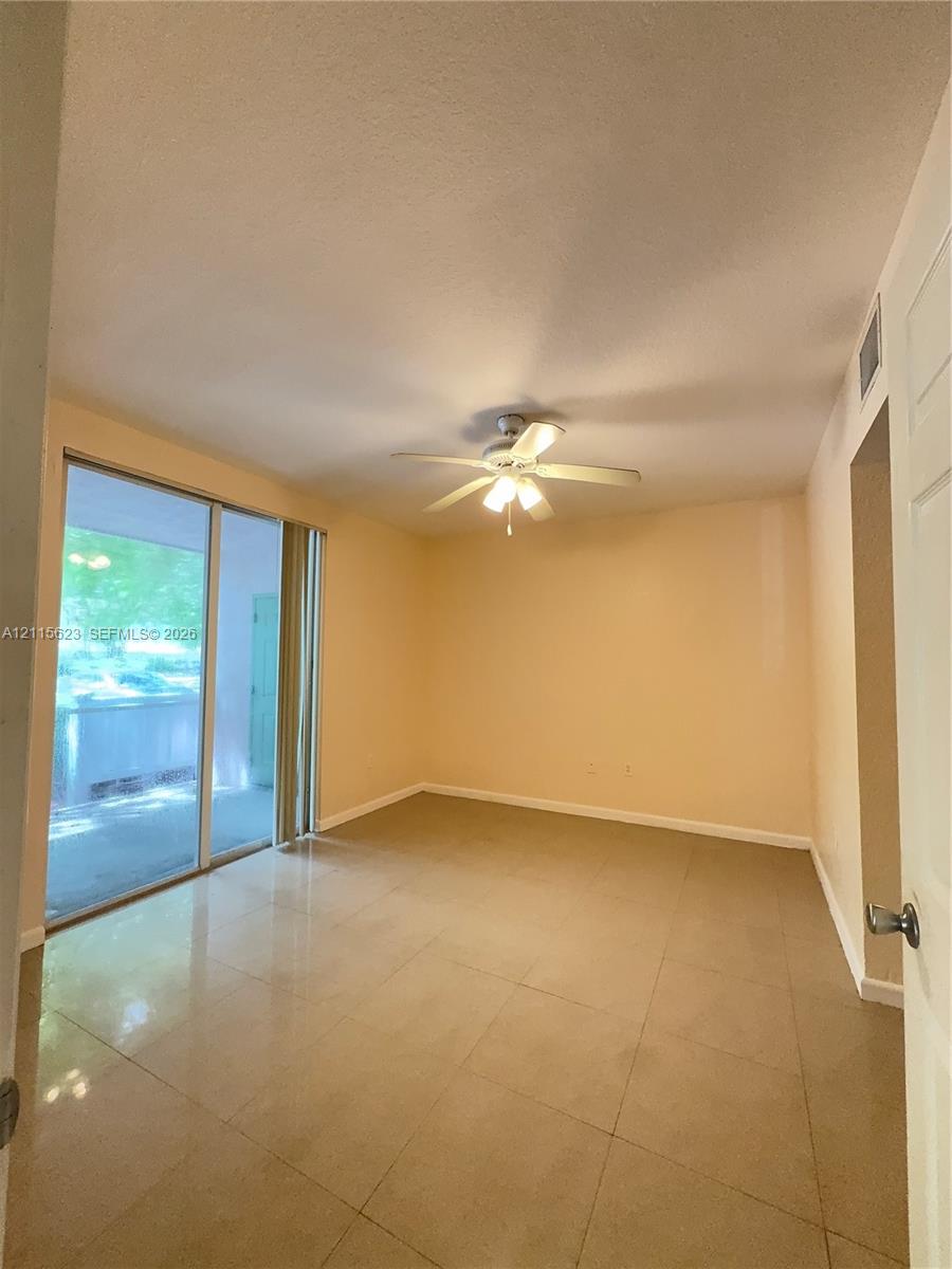 Large-format tile flooring, ceiling fan with integrated lighting, and sliding glass doors with direct access to an exterior patio
