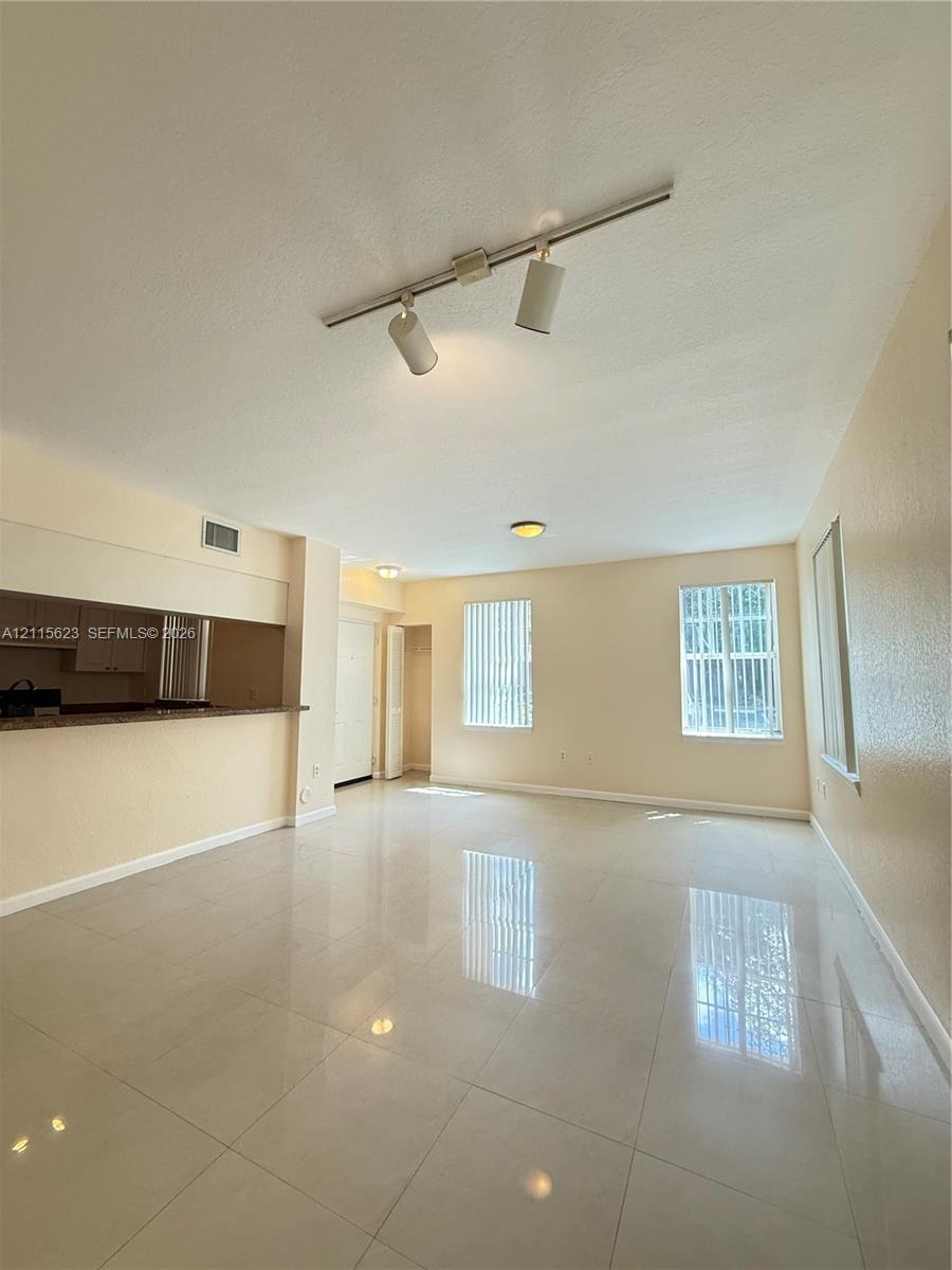 Open-concept living space featuring high-gloss tile flooring, adjustable track lighting, neutral wall finishes, and a pass-through service counter