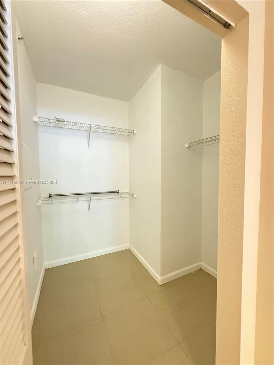 Storage space featuring white walls, large-format tile flooring, and tiered white wire shelving with integrated rods
