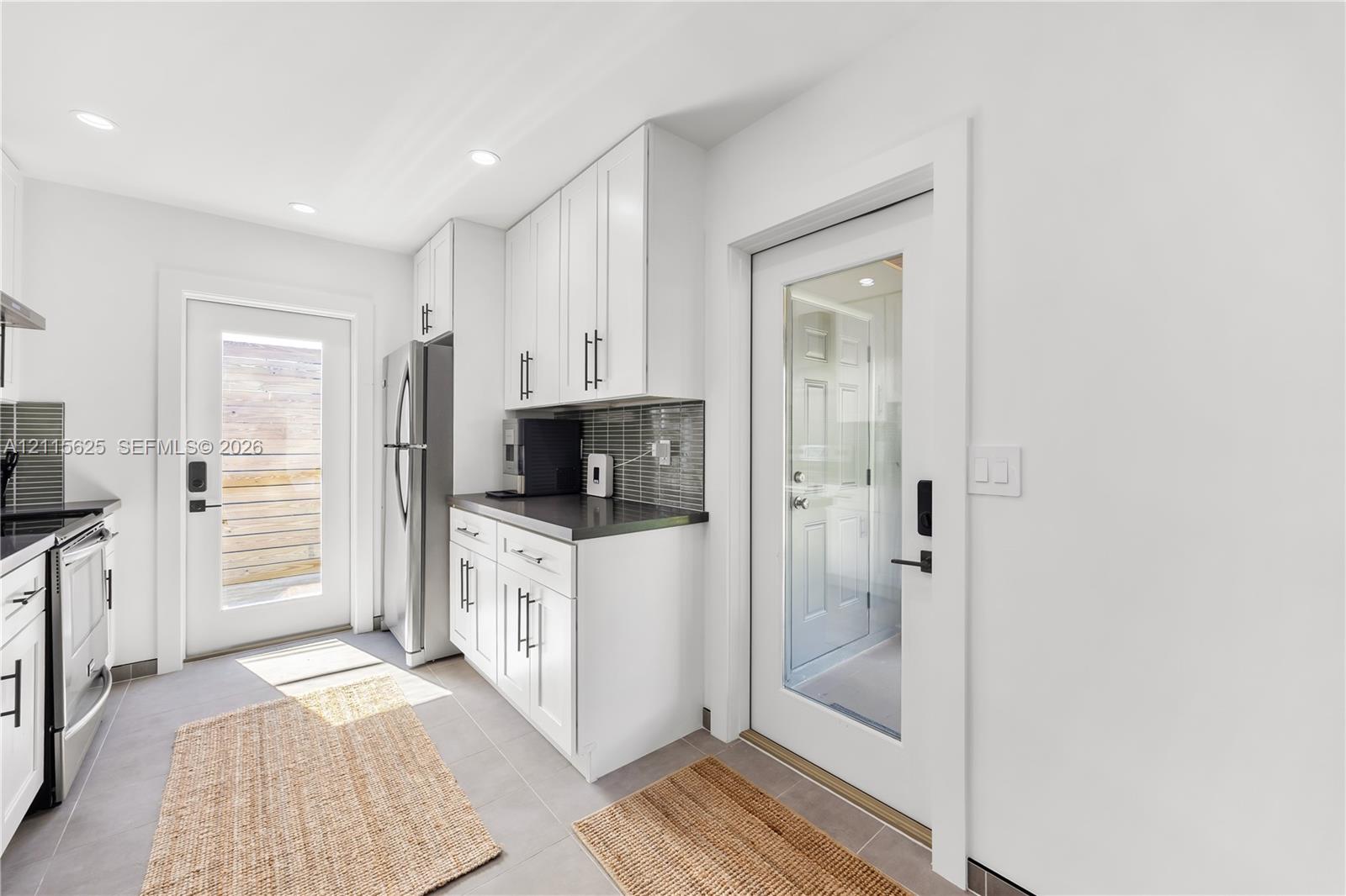 Kitchen featuring white shaker-style cabinetry, dark stone-finish countertops, tiled backsplash, stainless steel appliances, and glass-paneled exterior doors