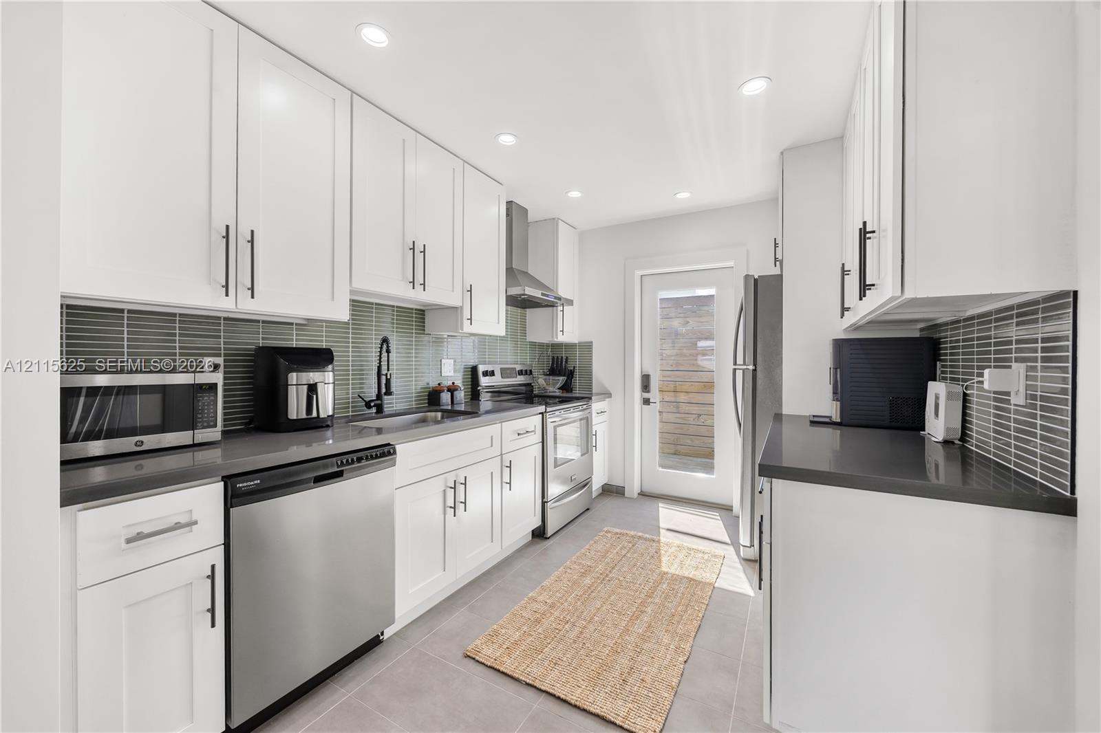 Kitchen featuring white shaker-style cabinetry, matte black hardware, stone-composite countertops, linear glass tile backsplash, and stainless steel appliances