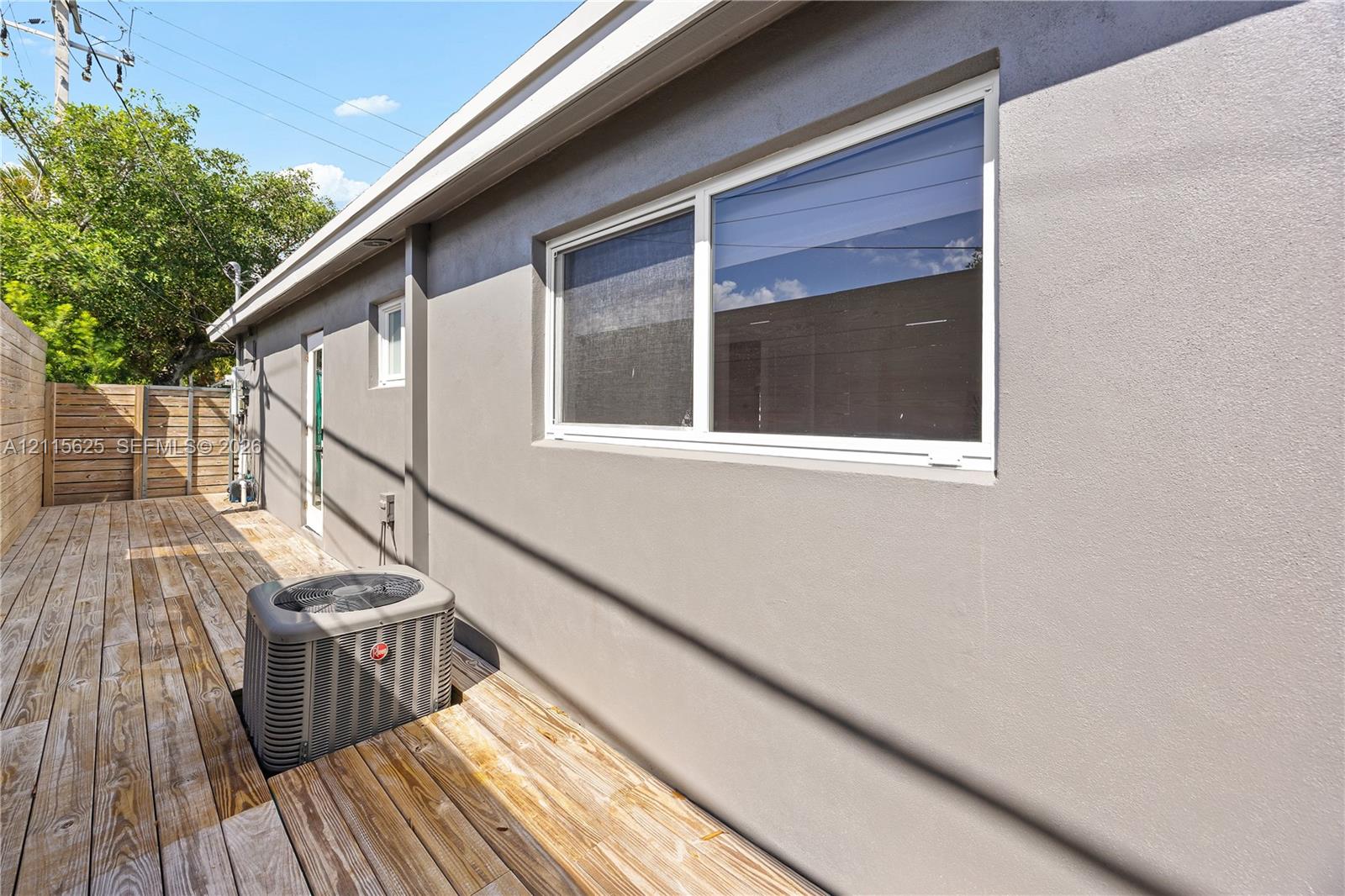 Exterior side space featuring wood-finish decking, smooth stucco siding, white-trimmed horizontal sliding windows, and a privacy fence