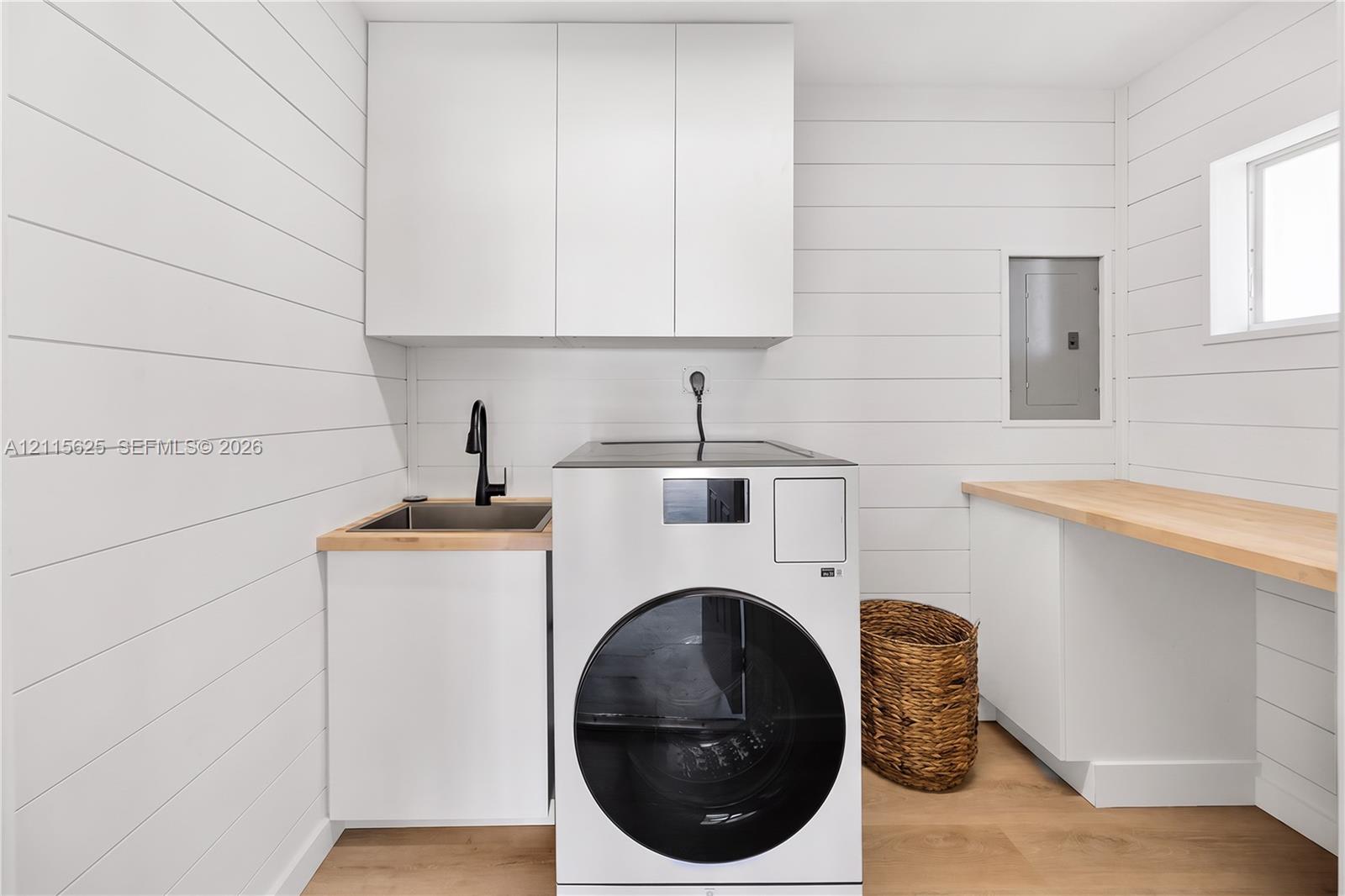 Laundry space featuring horizontal plank wall paneling, white built-in cabinetry, wood-finish countertops, an integrated drop-in sink with a matte black faucet, and wood-finish flooring