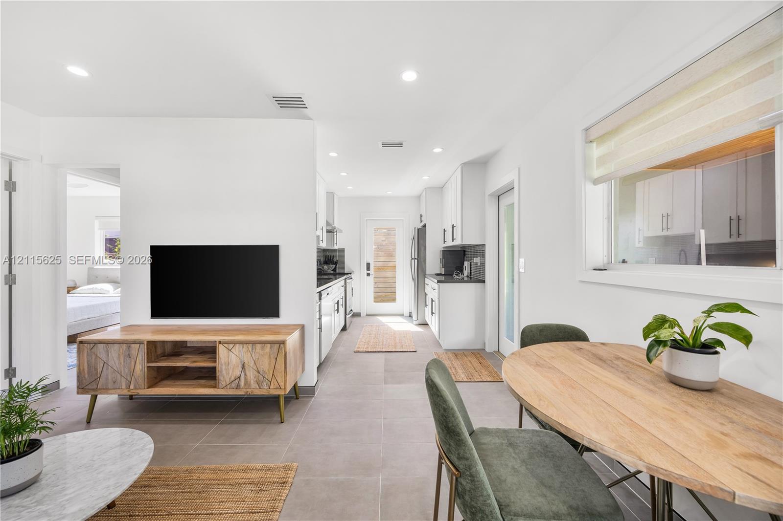 Open-concept interior featuring large-format tile flooring, recessed lighting, white cabinetry, and a full-light glass entry door