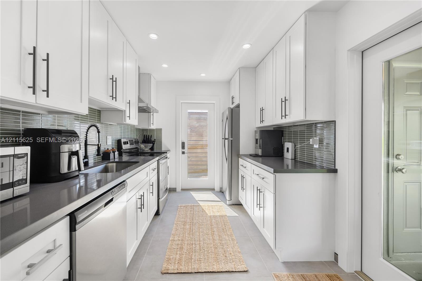 Kitchen featuring white shaker-style cabinetry, dark stone countertops, horizontal glass tile backsplash, stainless steel appliances, and recessed lighting
