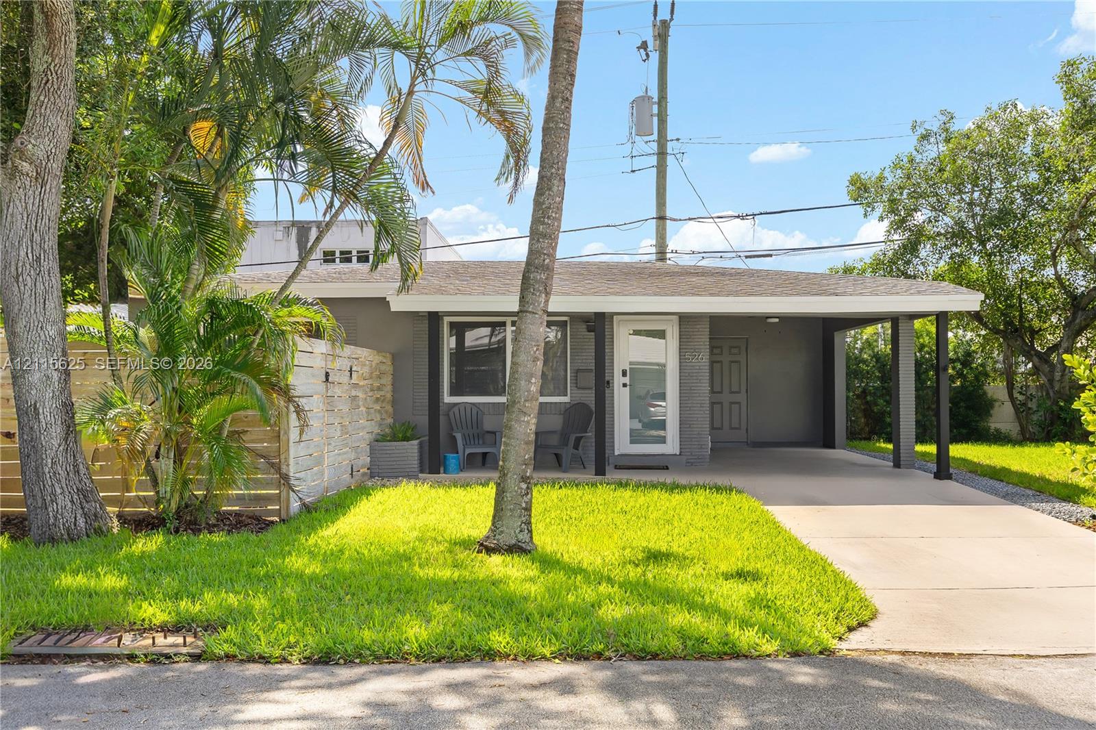 Single-story residence featuring a paved carport, covered front entry, horizontal wood-slat privacy fencing, and mature palm trees