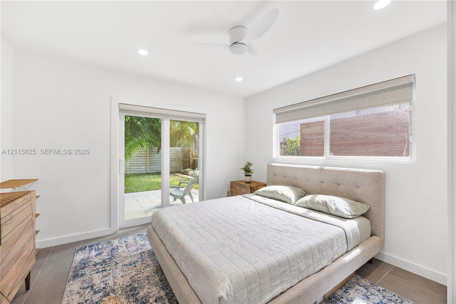 Neutral-toned interior featuring large-format tile flooring, recessed lighting, a modern ceiling fan, sliding glass door, and a horizontal window with a roller shade