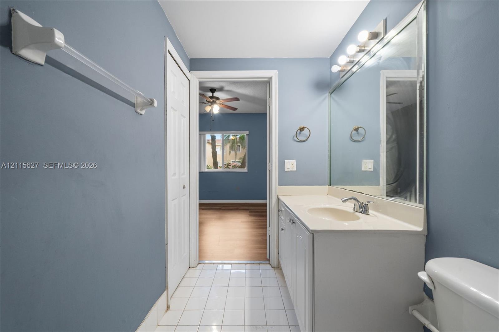 Bathroom featuring a white vanity cabinet with an integrated sink, a full-width wall mirror, chrome fixtures, and white tile flooring