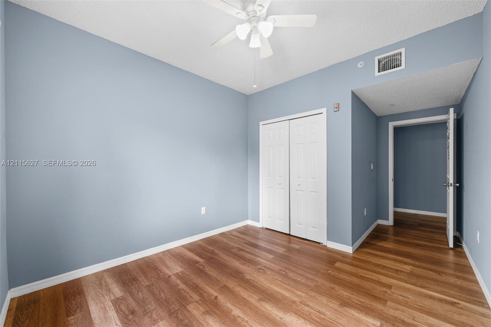 Room featuring wood-finish flooring, a ceiling fan with integrated lighting, and a double-door closet