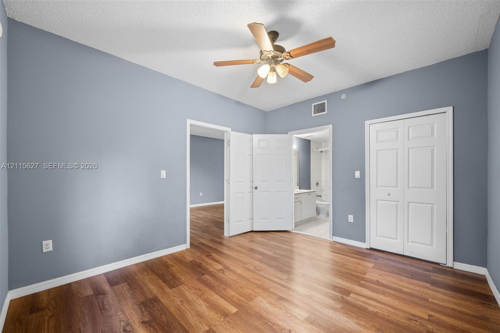 Room featuring wood-finish flooring, a ceiling fan with integrated lighting, dual-panel interior doors, and a double-door closet