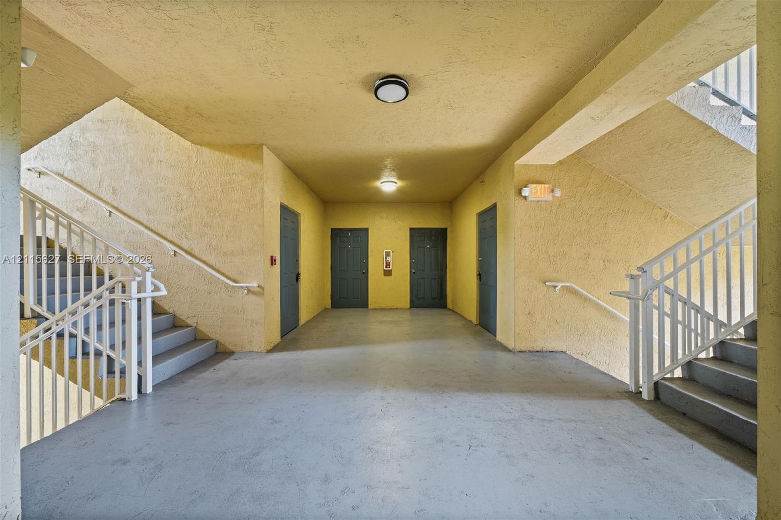 Covered common area featuring textured walls, solid surface flooring, dual staircases with metal railings, and flush-mount ceiling lighting