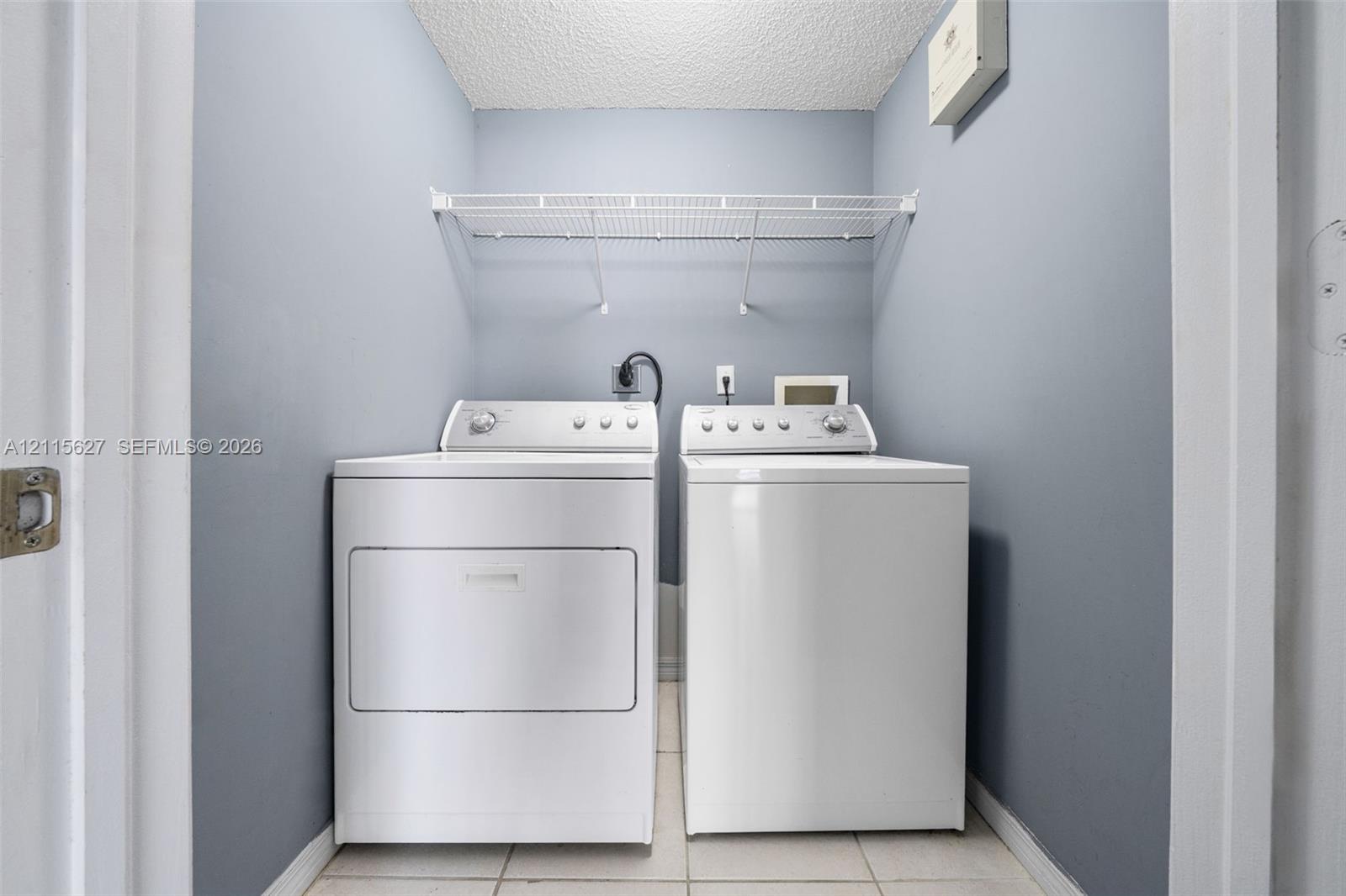 Dedicated laundry alcove featuring tile flooring and overhead wire shelving