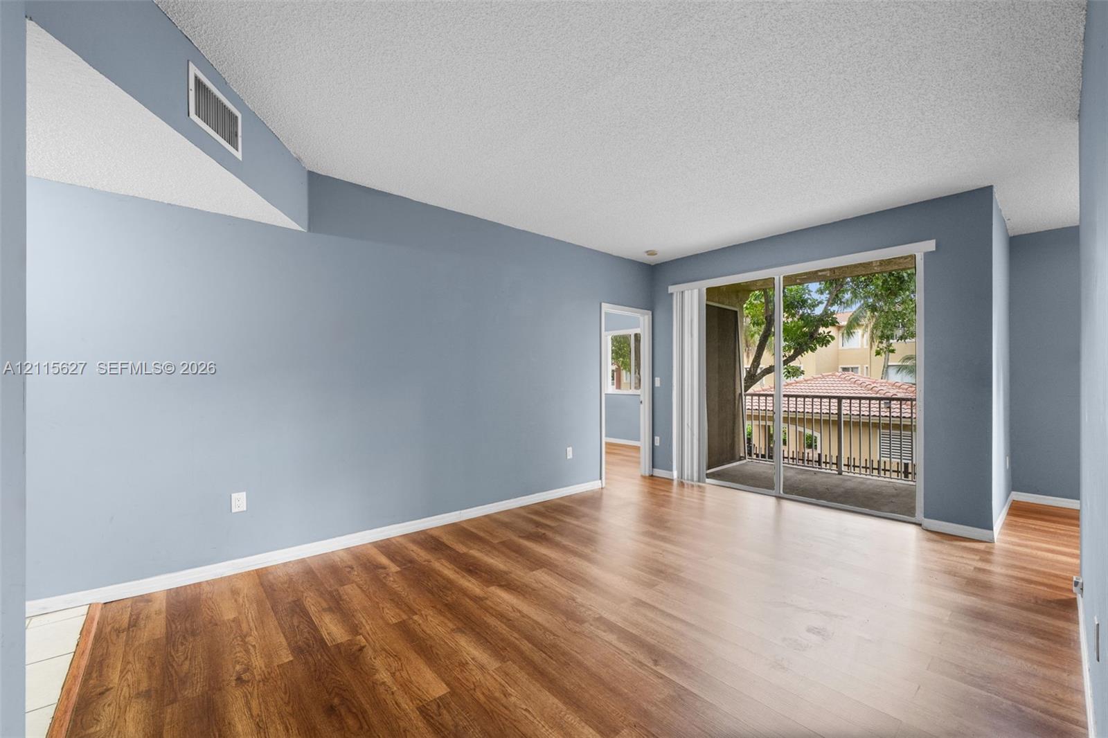 Living area featuring wood-finish flooring, vaulted ceiling, and sliding glass doors leading to a private balcony