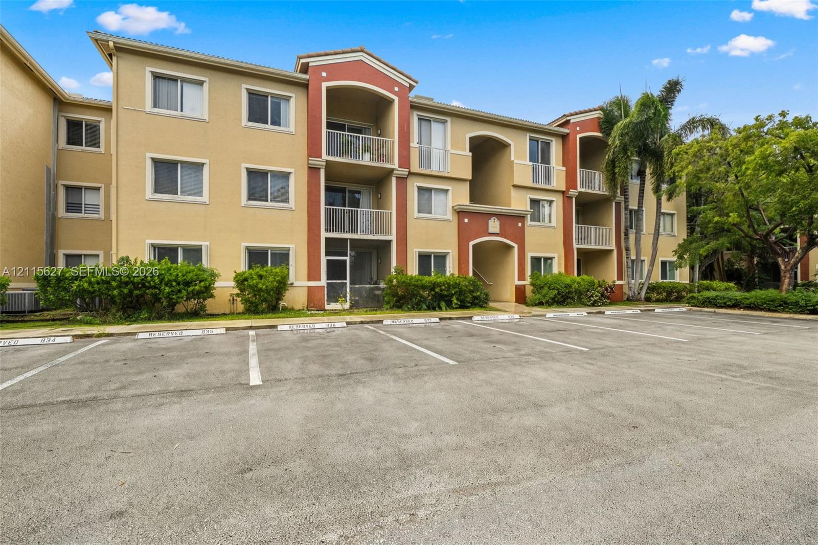 Multi-story residential building featuring stucco exterior, private covered balconies, and dedicated surface parking