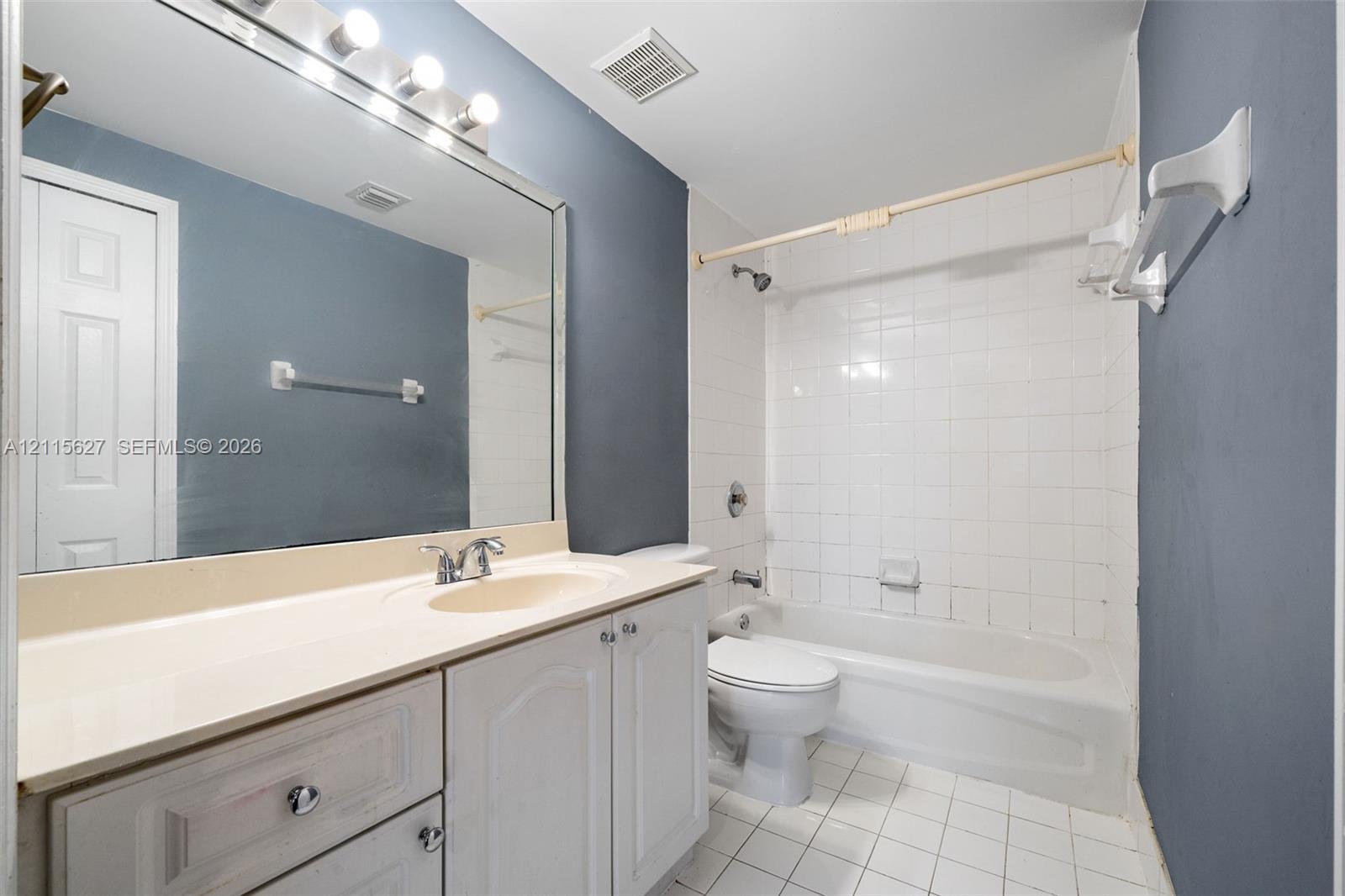 Bathroom featuring white cabinetry, integrated sink, vanity-width wall mirror, chrome-finish plumbing fixtures, and a tiled tub surround