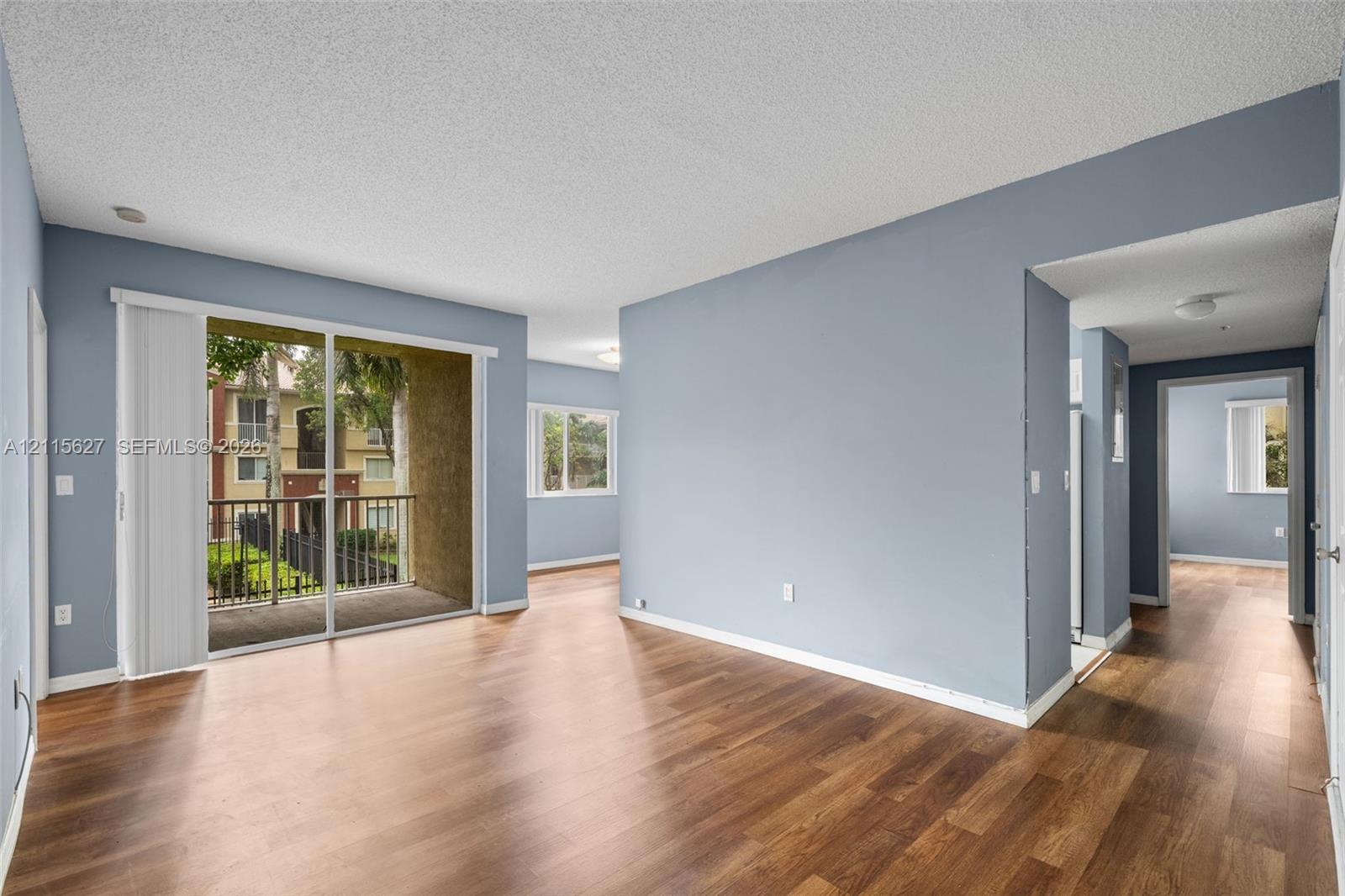 Open-concept interior featuring wood-finish flooring, sliding glass door access to a private balcony, and neutral paint palette