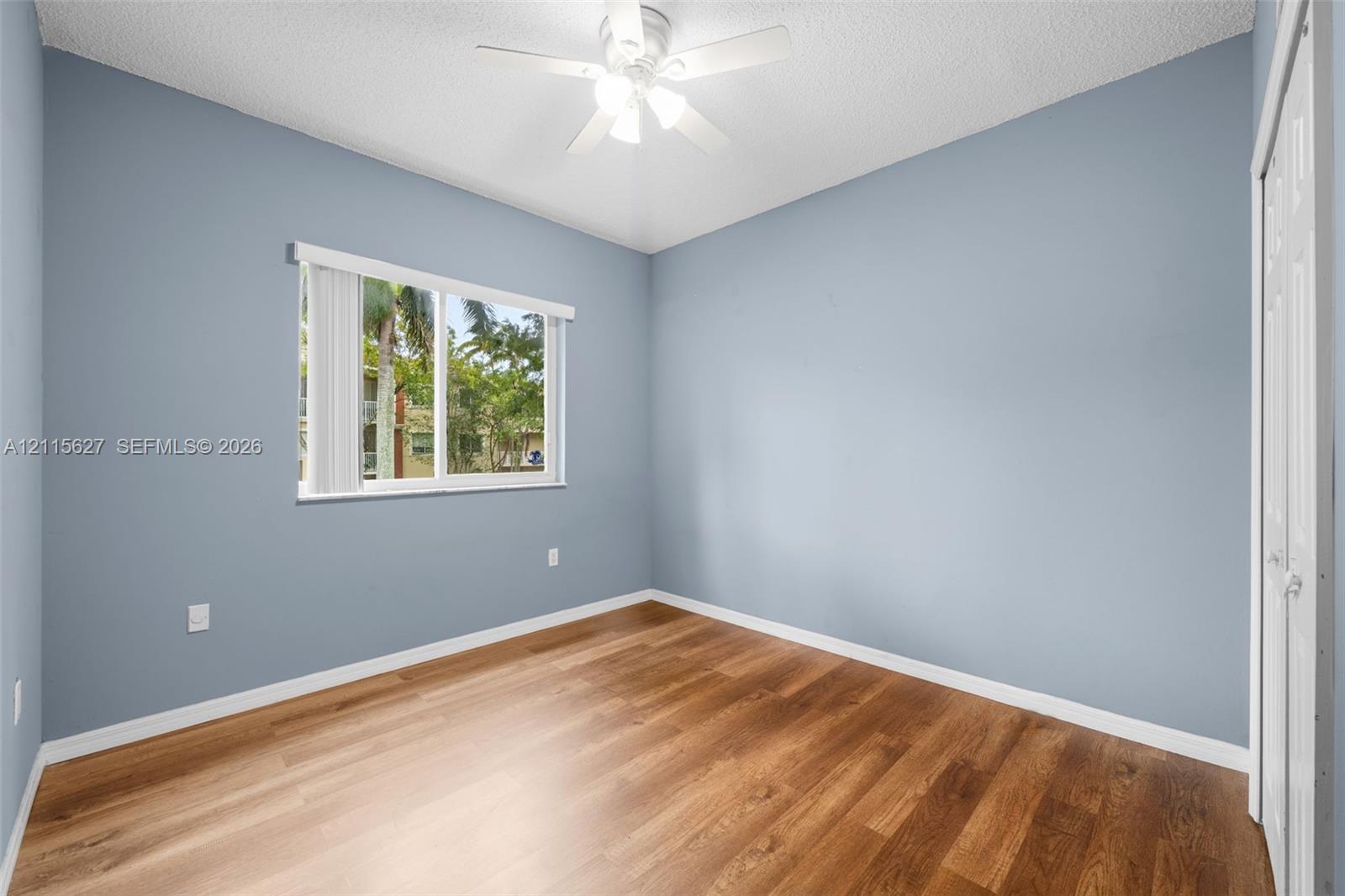 Room featuring wood-finish flooring, light blue wall paint, a ceiling fan with integrated lighting, and a white sliding-door closet