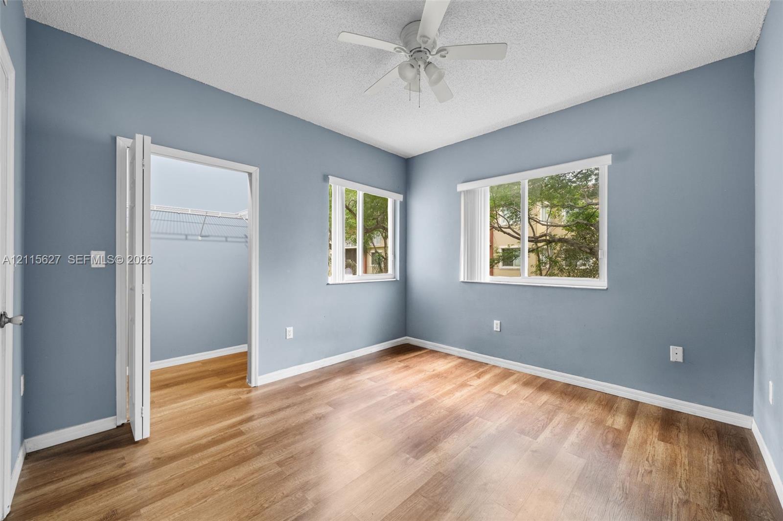 Room featuring wood-finish flooring, two windows, a ceiling fan with integrated lighting, and a closet with bifold doors