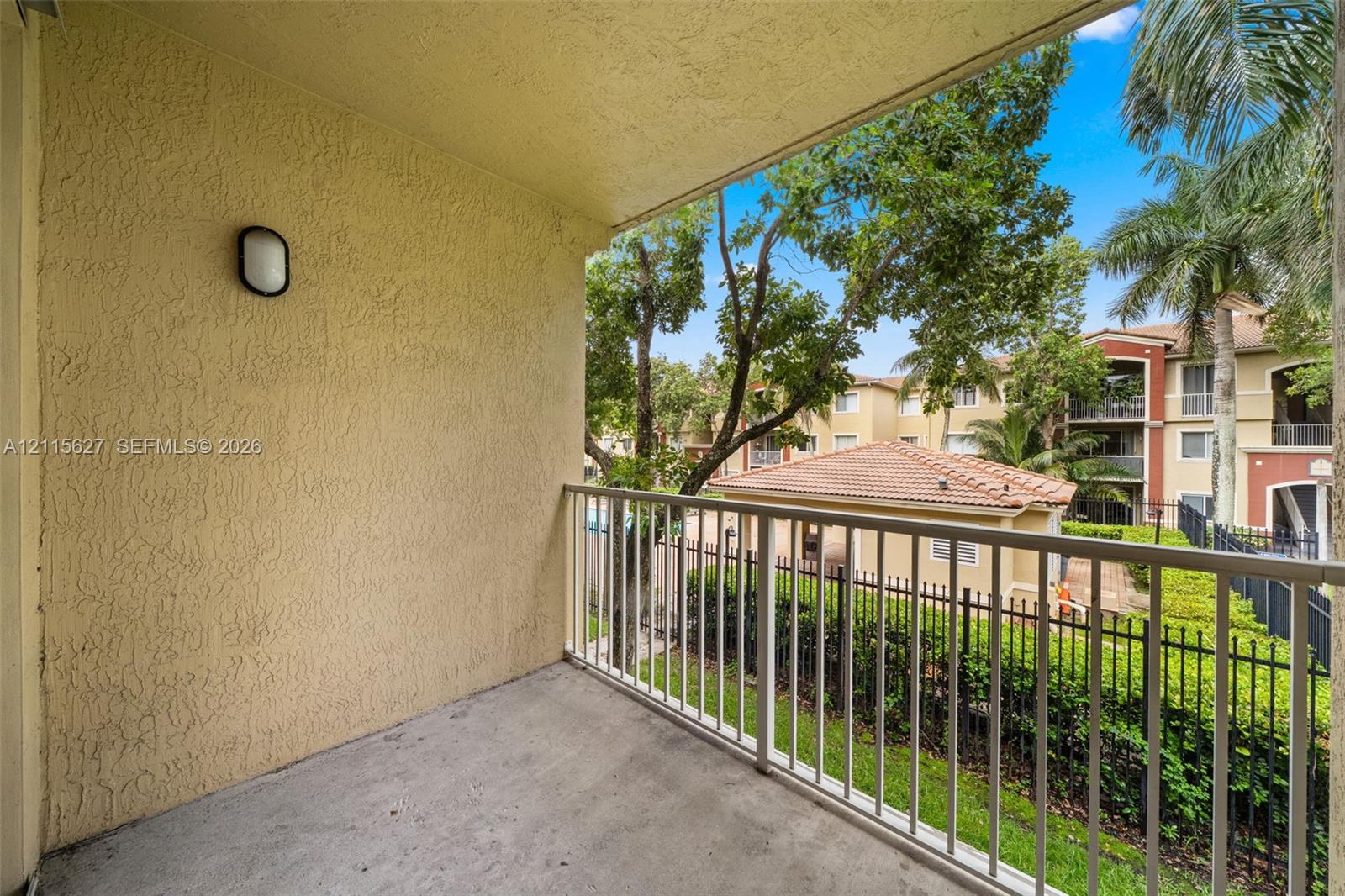Private balcony featuring a concrete floor, textured stucco walls, an attached wall-mounted light fixture, and a metal railing