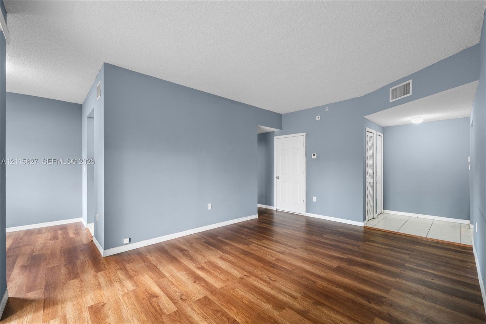 Open-concept interior featuring wood-finish flooring, textured ceiling, six-panel interior doors, and neutral wall tones