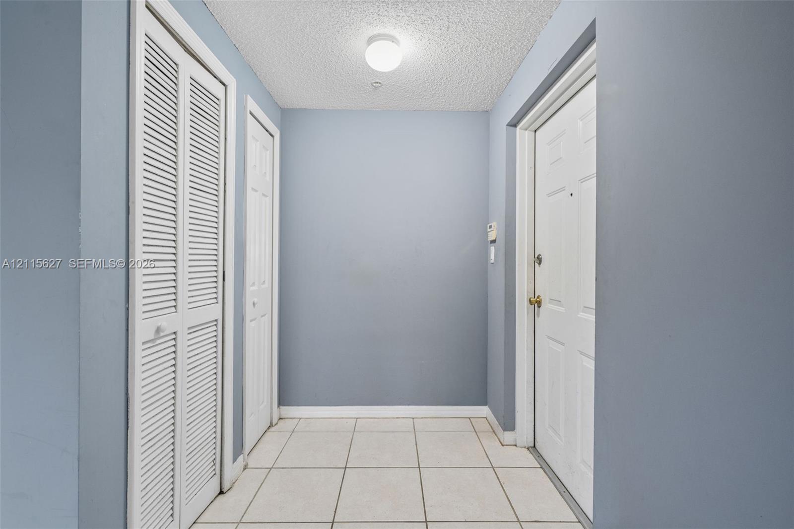 Entryway featuring white tile flooring, louvered bi-fold closet doors, a paneled interior door with metal hardware, and a ceiling-mounted light fixture