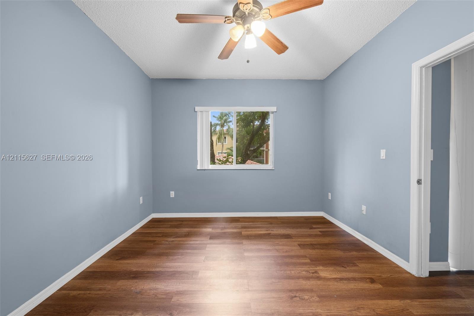 Wood-finish flooring, ceiling fan with integrated lighting, and a window with exterior scenery