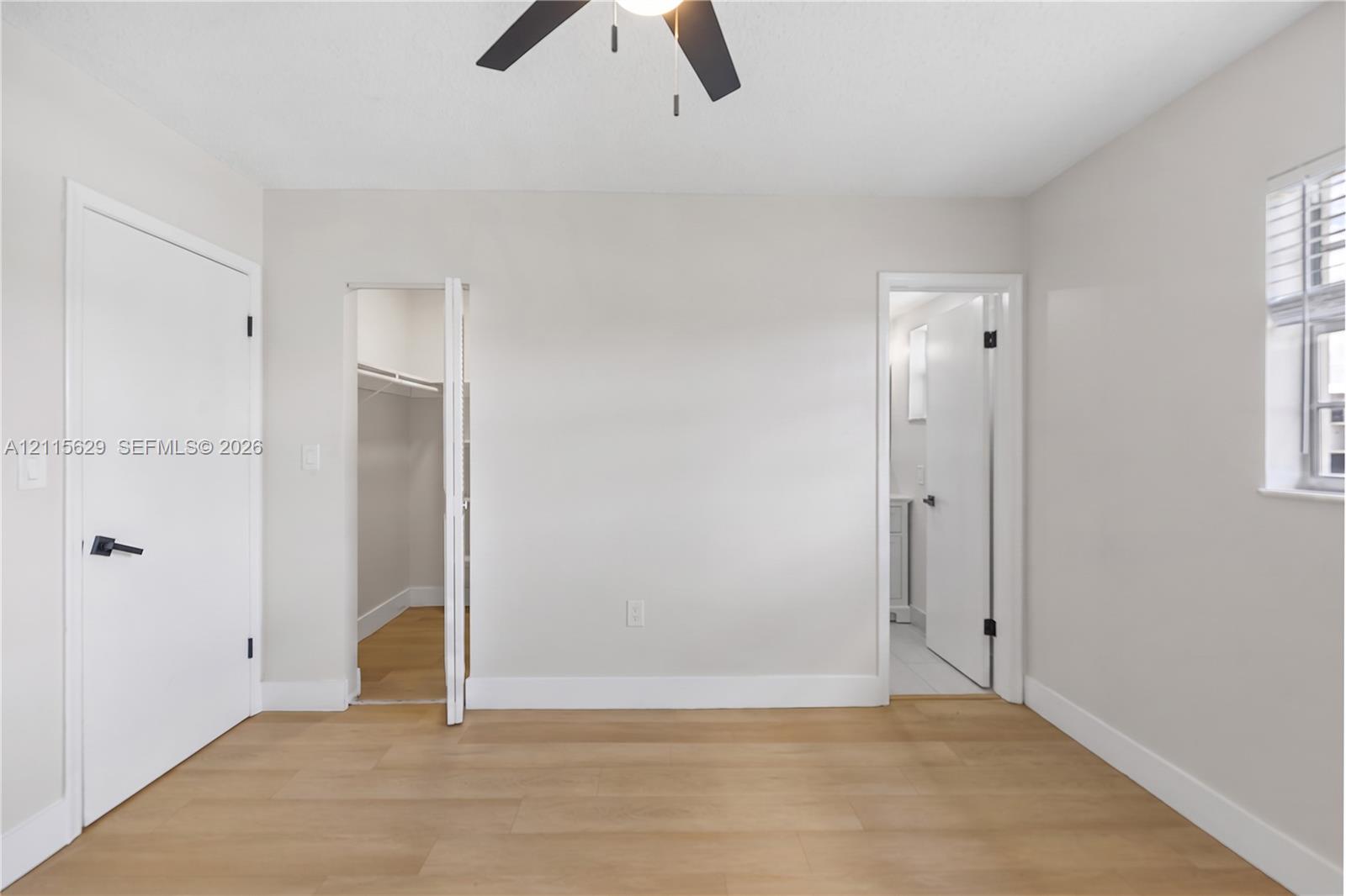 Room featuring light wood-finish flooring, matte black hardware, recessed closet storage, and a ceiling-mounted fan with integrated lighting
