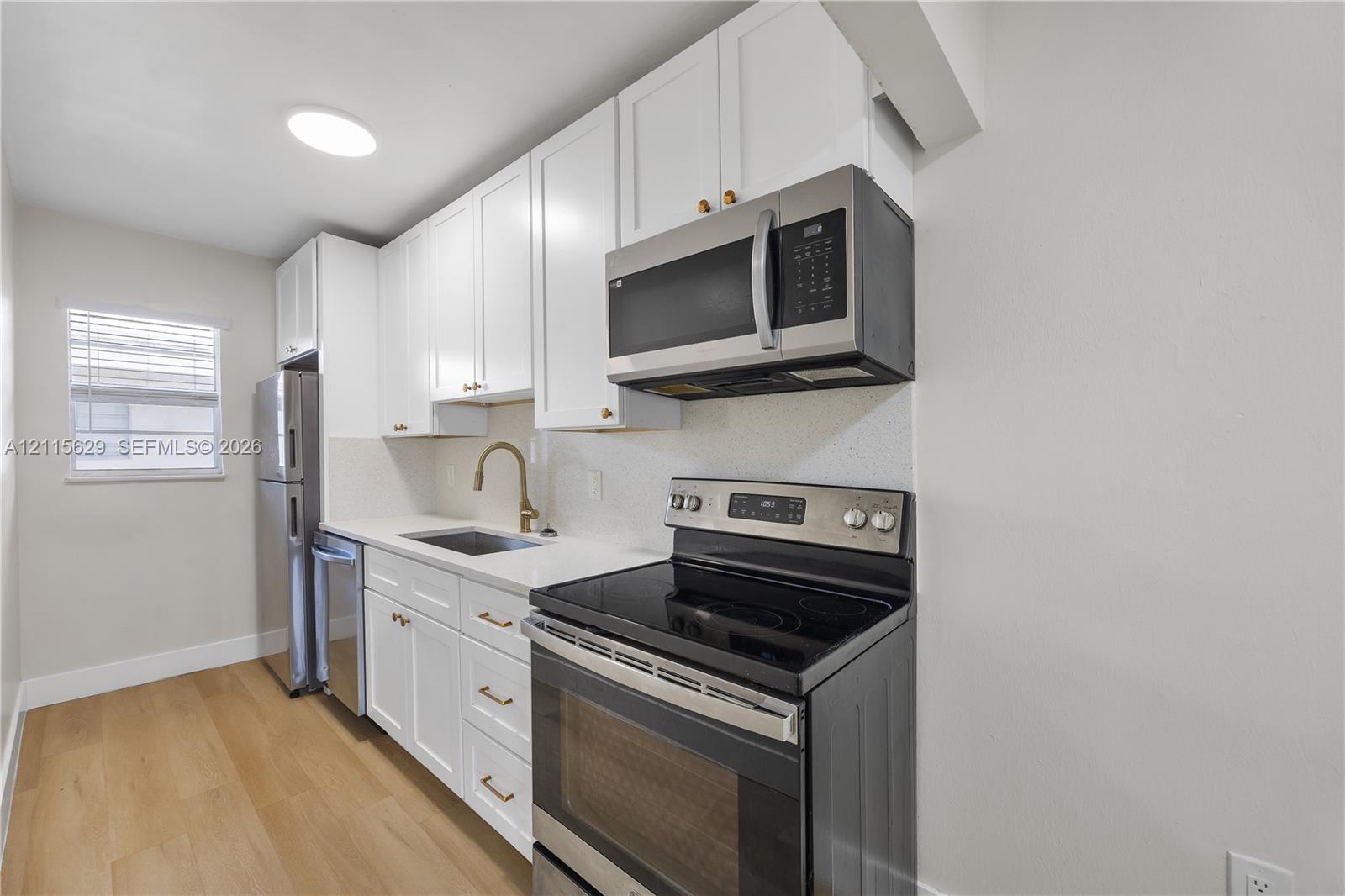 Kitchen featuring white cabinetry, wood-finish flooring, stainless steel appliances, a brass-tone faucet, and stone-surface countertops