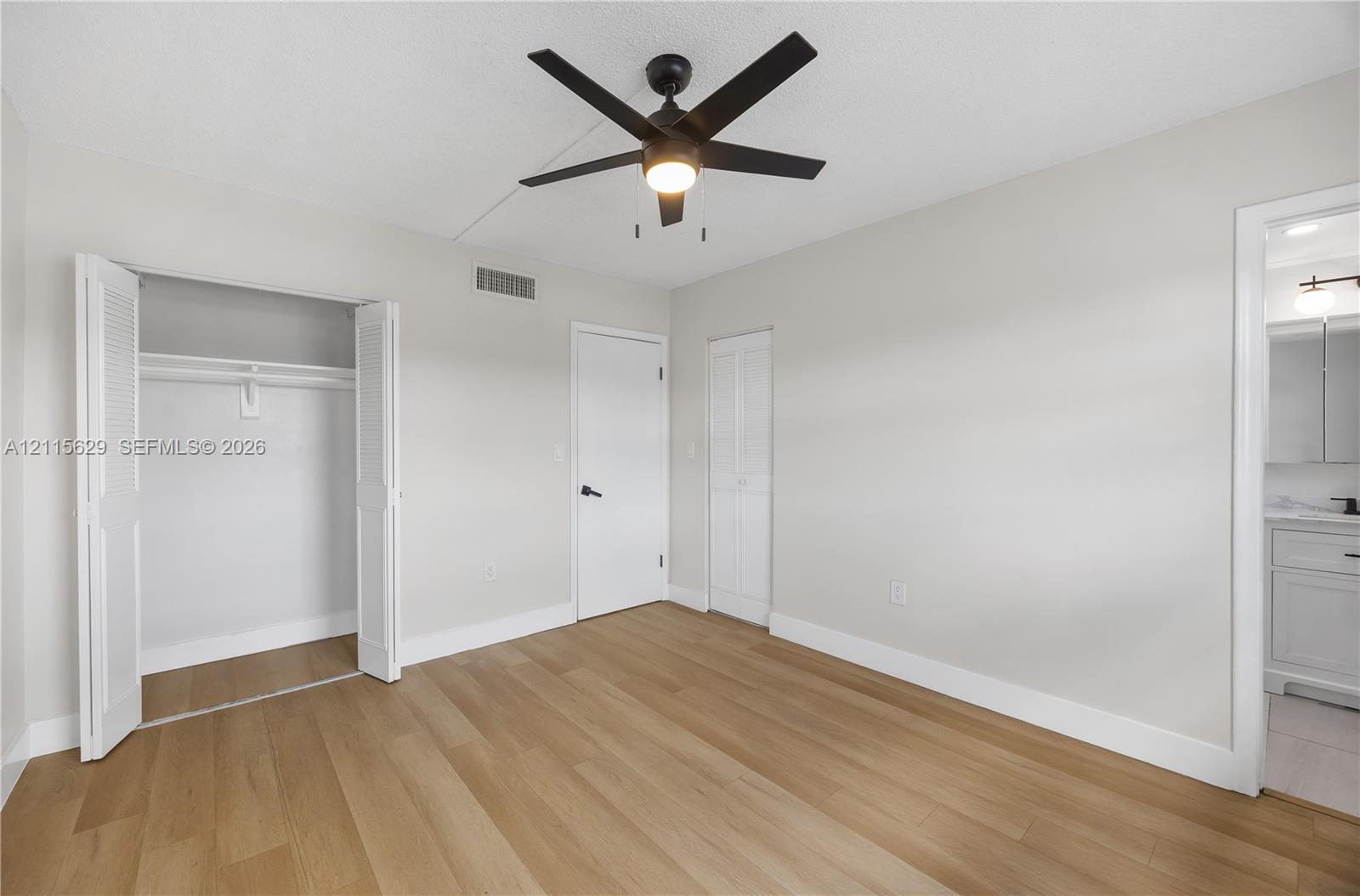 Interior space featuring wood-finish flooring, a matte black multi-blade ceiling fan with integrated lighting, bi-fold closet doors, and neutral wall tones
