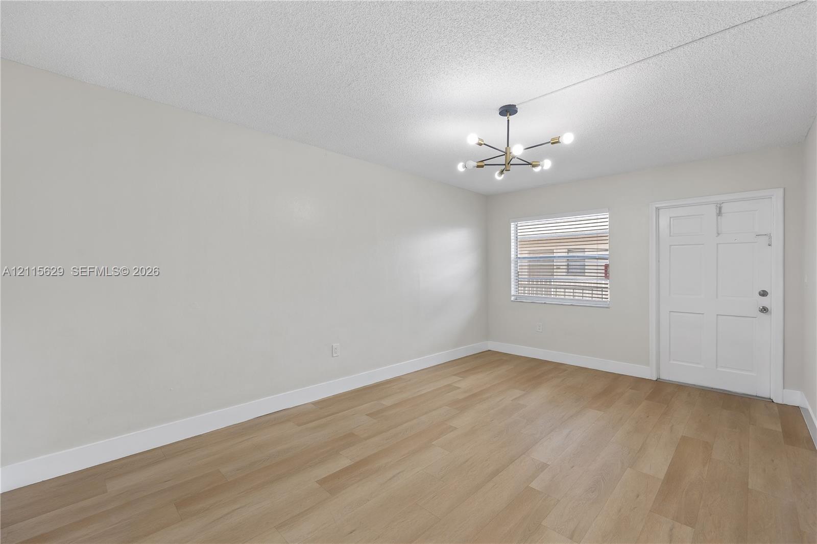 Neutral-toned interior featuring wood-finish flooring, a multi-arm modern pendant light fixture, and a white six-panel door