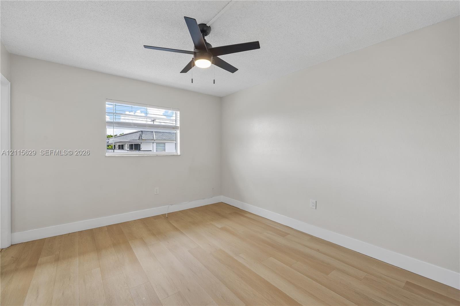 Neutral-toned room featuring light wood-finish flooring, a ceiling fan with integrated lighting, and horizontal window blinds