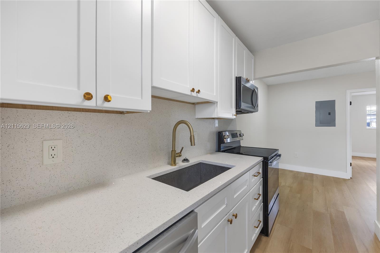 Kitchen featuring white shaker-style cabinetry, solid-surface countertops, gold-tone hardware, a gooseneck faucet with an undermount sink, and wood-finish flooring