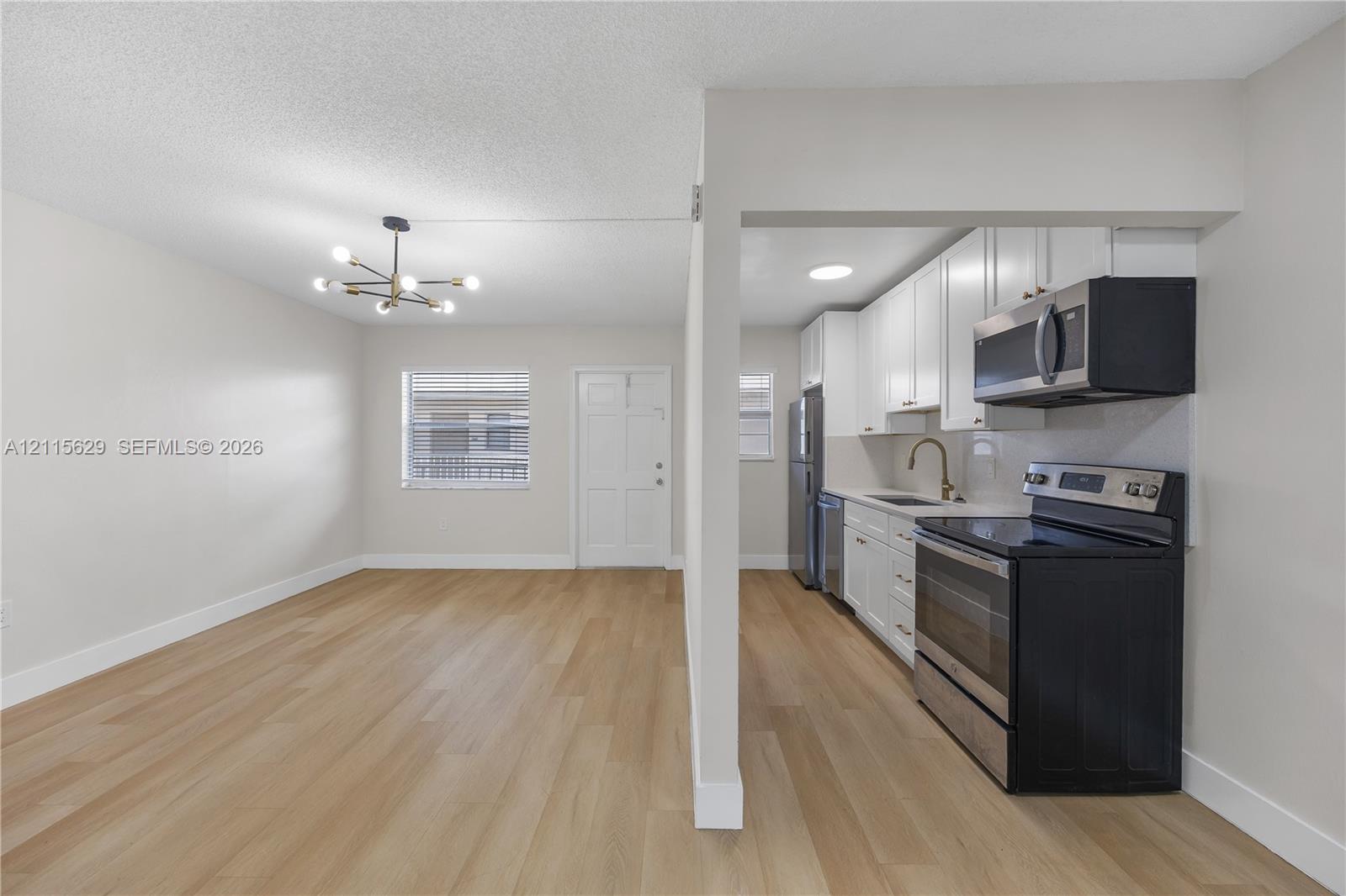 Wood-finish flooring, white shaker-style cabinetry, stainless steel appliances, multi-arm sputnik-style chandelier, and recessed lighting