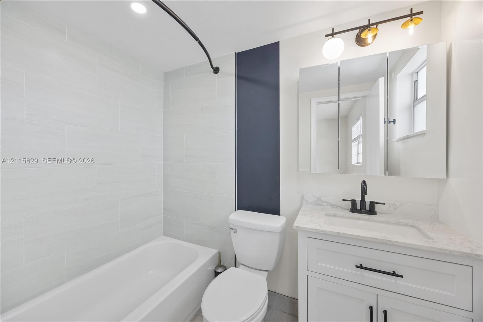 Bathroom featuring a white vanity with stone-finish countertop, matte black hardware, integrated vanity mirror with cabinetry, and tub-shower combination with light-toned wall tile