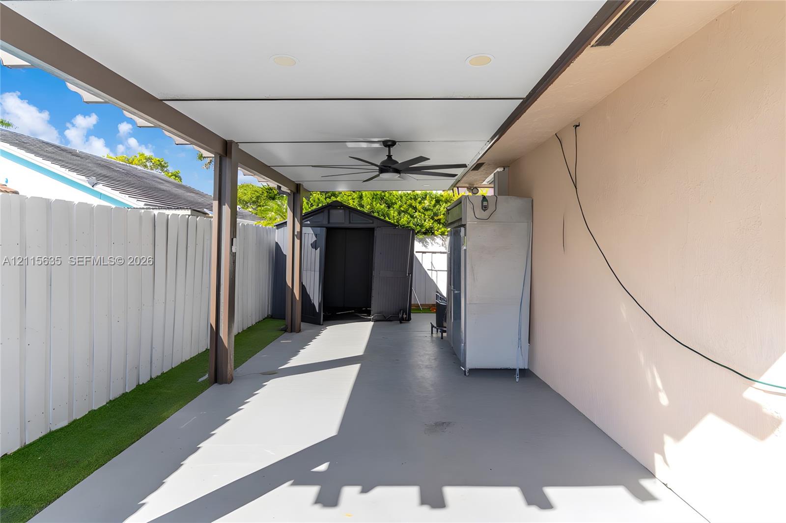 Covered patio featuring a concrete floor, recessed lighting, and a ceiling fan, enclosed by a white vertical fence