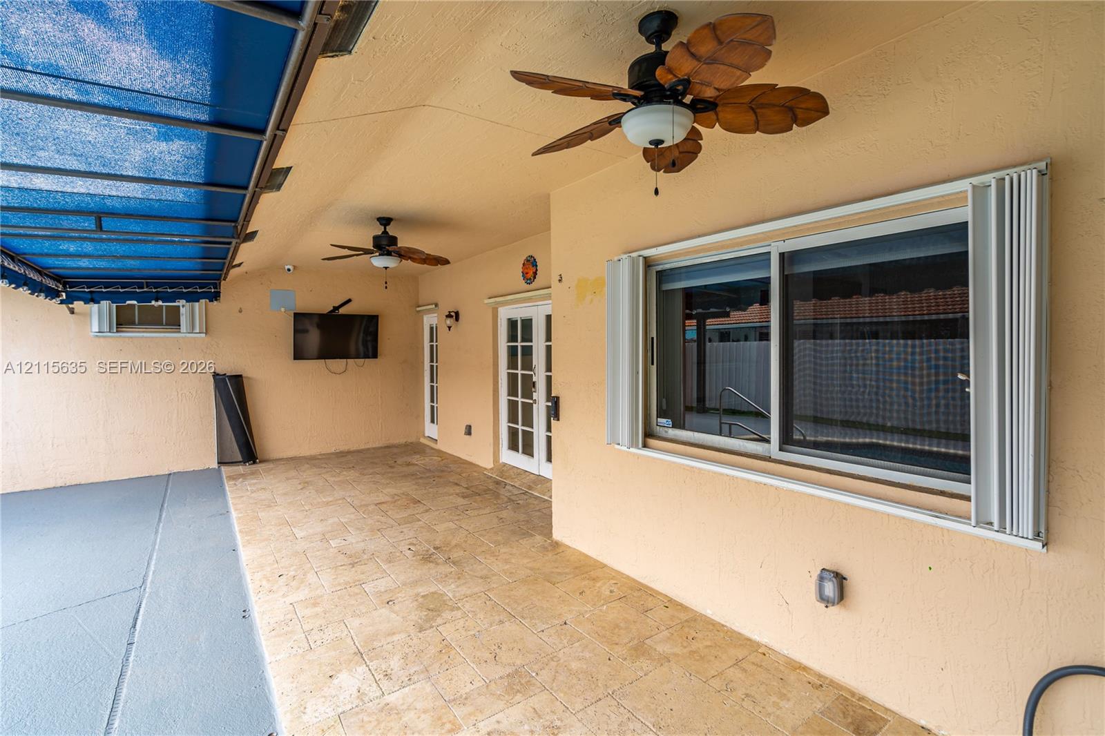 Covered patio featuring stone-tiled flooring, dual ceiling fans, a retractable blue canopy, and sliding glass entry doors