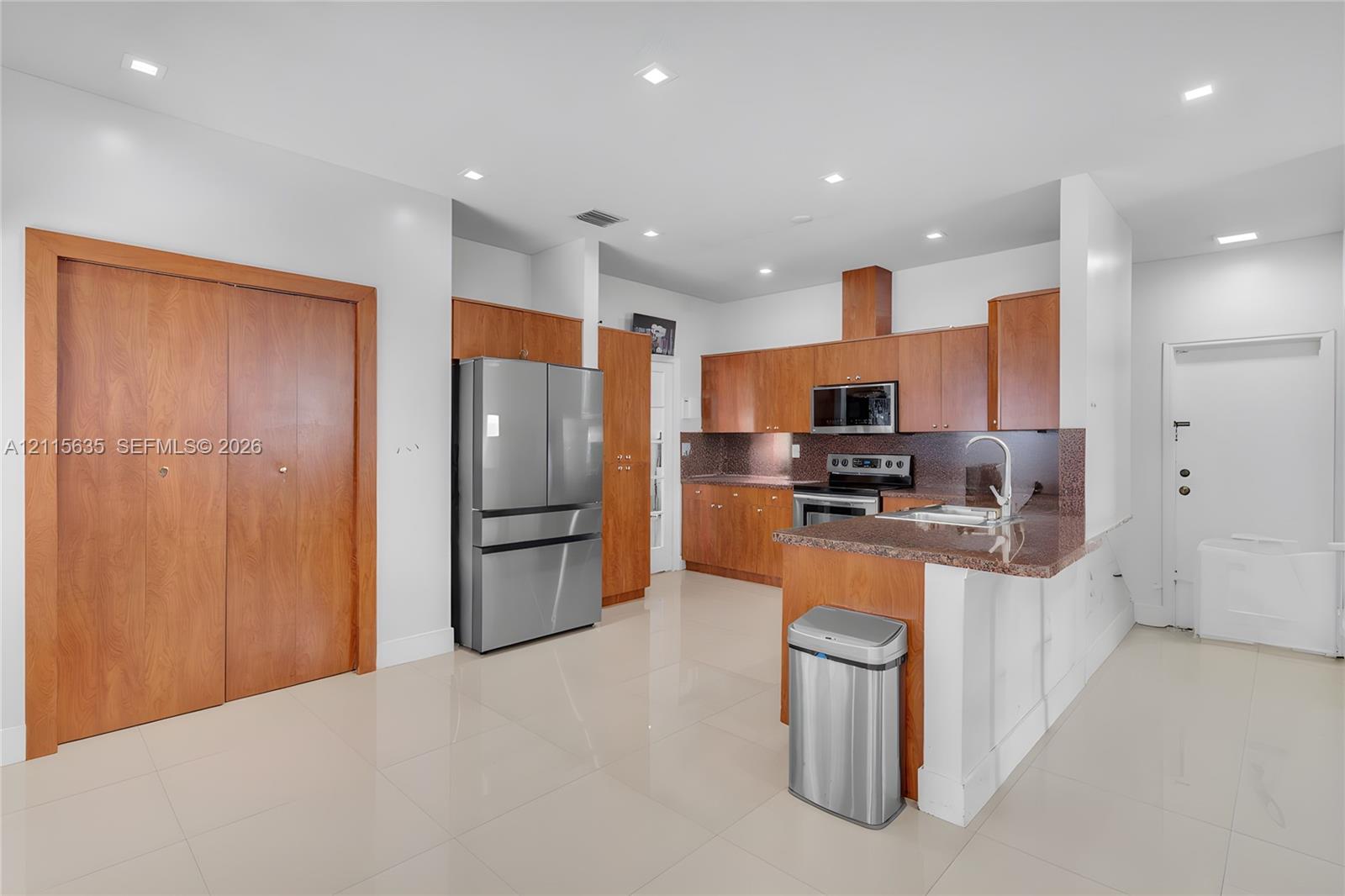 Kitchen featuring wood cabinetry, stone countertops, stainless steel appliances, tile flooring, and recessed ceiling lighting