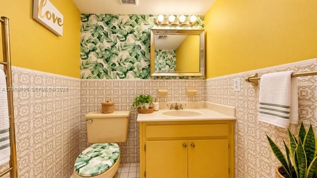 Custom vanity featuring a neutral countertop with an integrated basin, decorative wall tile wainscoting, and a metallic four-light vanity fixture