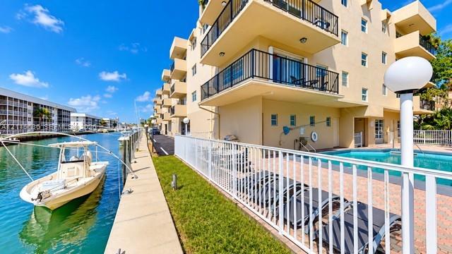 Waterfront building exterior featuring private boat slips, an in-ground pool with paved deck, and cantilevered balconies with black railings