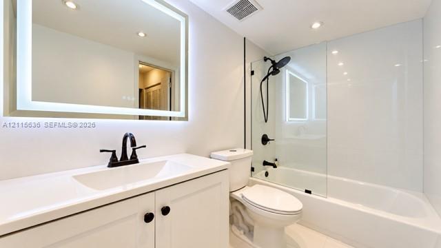 Bathroom featuring an illuminated wall-mounted mirror, white cabinetry with a solid surface countertop, matte black faucet hardware, and a tub-shower combination with a glass panel enclosure