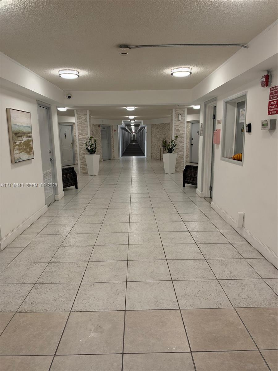 Interior corridor featuring neutral tile flooring, stone-accented structural columns, and recessed lighting