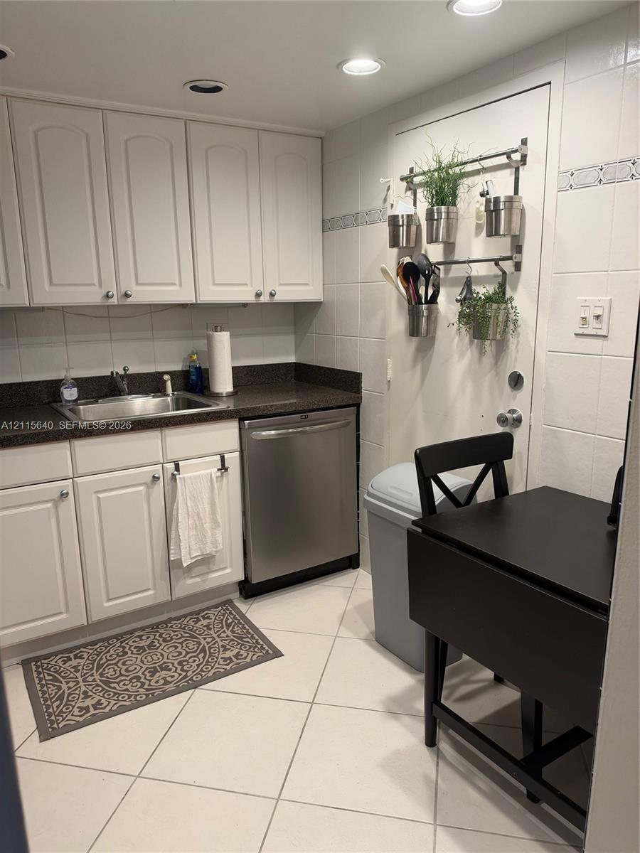 Kitchen featuring white cabinetry, dark stone-finish countertops, an undermount stainless steel sink, a stainless steel dishwasher, and tile flooring