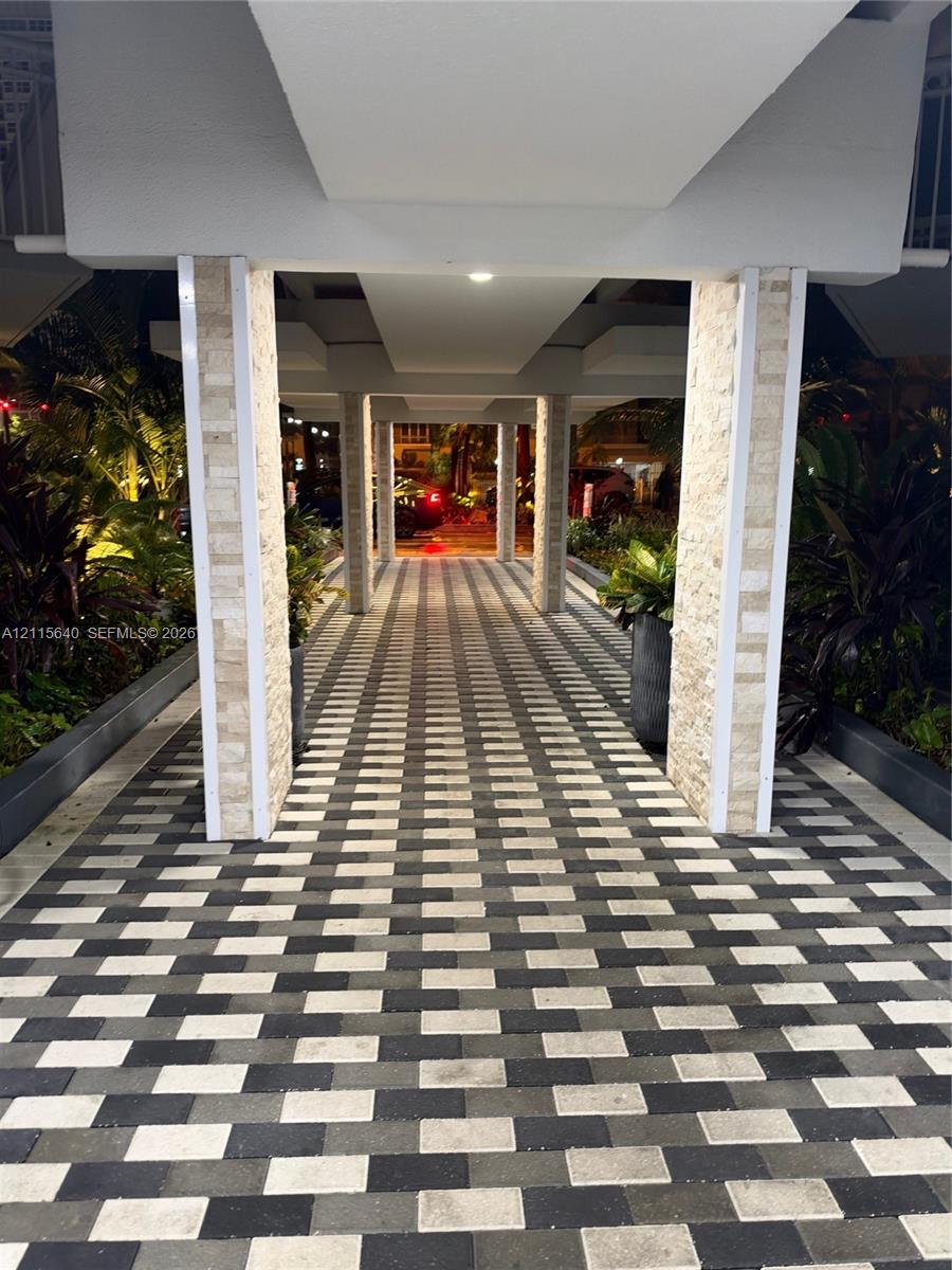 Covered walkway featuring a geometric paver path, tiered stone-cladding columns, and integrated recessed ceiling lighting