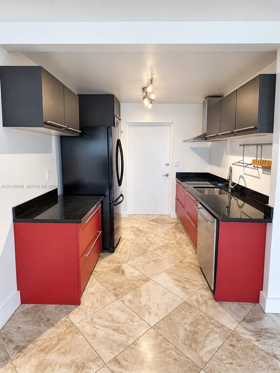 Kitchen featuring red and black flat-panel cabinetry, dark stone countertops, stainless steel appliances, and diagonal-pattern tile flooring