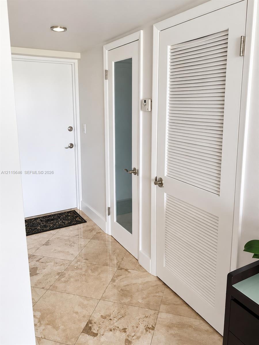 Diagonal-set stone tile flooring, white-finished interior doors with brushed nickel hardware, integrated louvered closet door, and recessed ceiling lighting