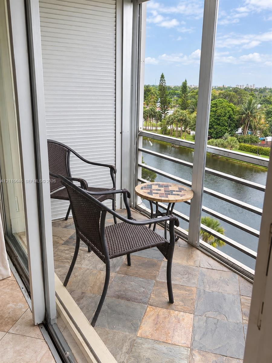 Covered balcony featuring multi-tonal stone tile flooring, metal railing, and retractable shutter system