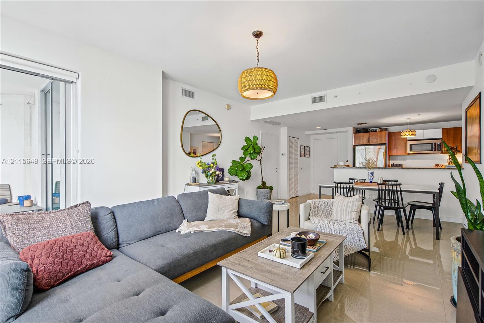 Open-concept interior featuring large-format tile flooring, a kitchen with wood-finish cabinetry, a breakfast bar, and a woven pendant light fixture