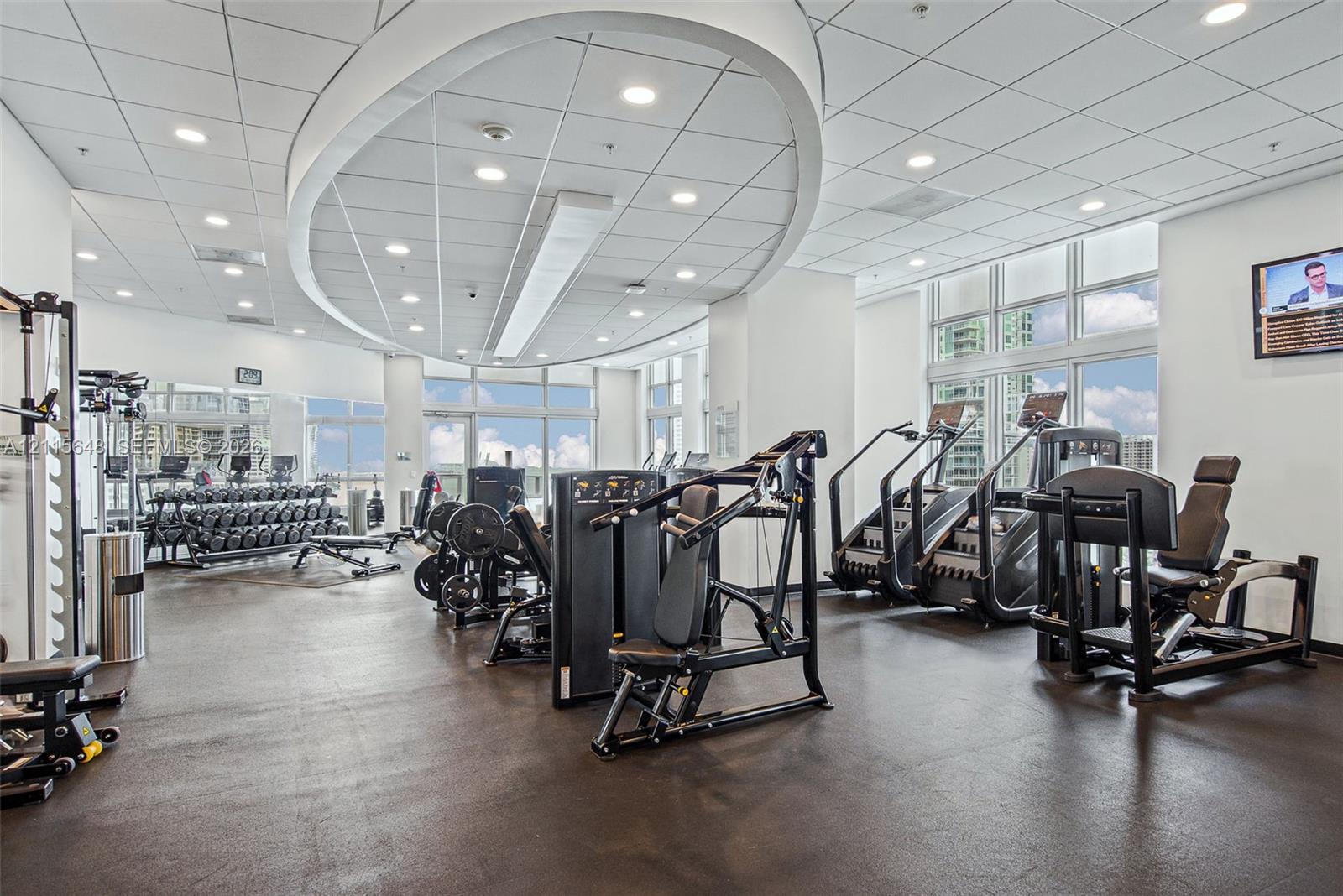 Fitness center featuring high ceilings with custom circular recessed lighting, rubberized flooring, and floor-to-ceiling windows